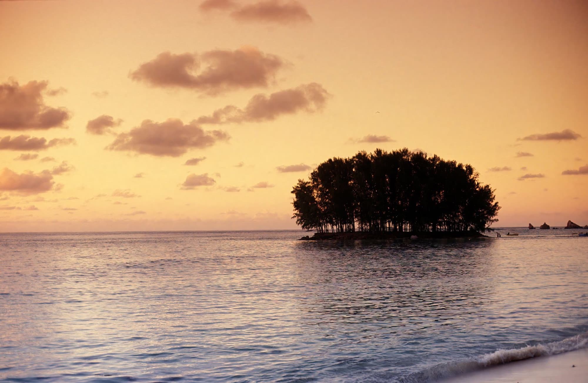 A tranquil sunset view of a small island silhouetted against the orange sky at La Digue, Seychelles.