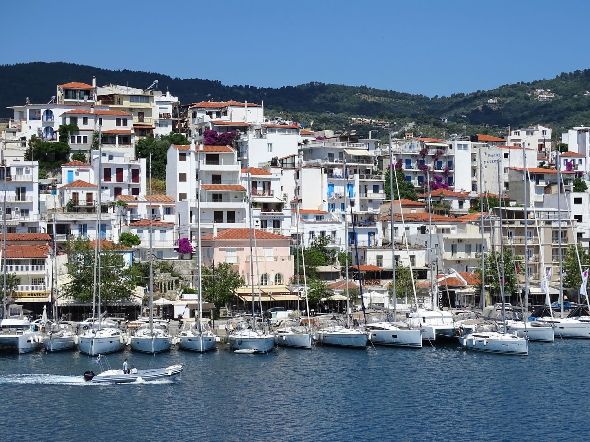 Colorful harbor scene in Skiathos, Greece, with docked sailboats against lush hills.