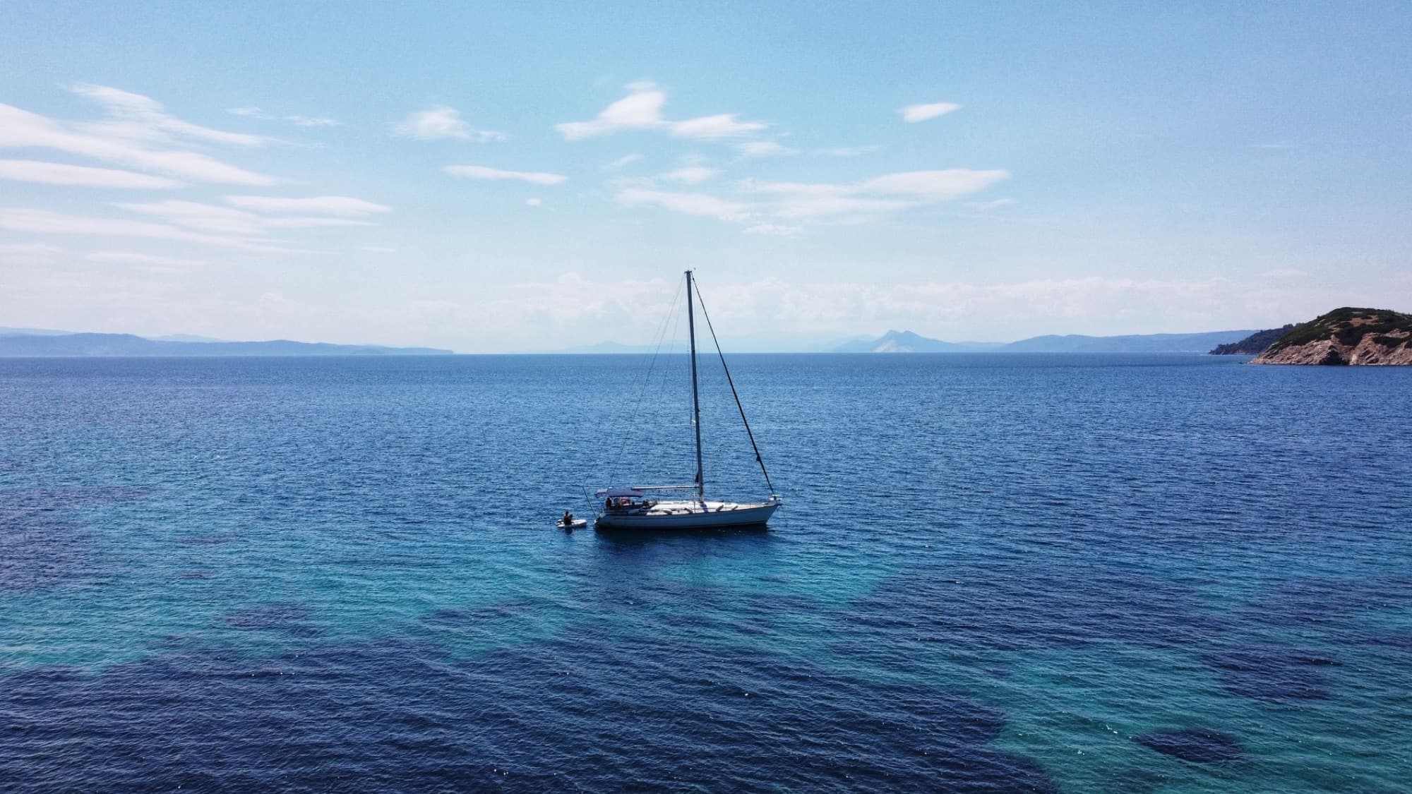 A peaceful sailboat floating on the clear blue waters near Skiathos, Greece on a sunny day.