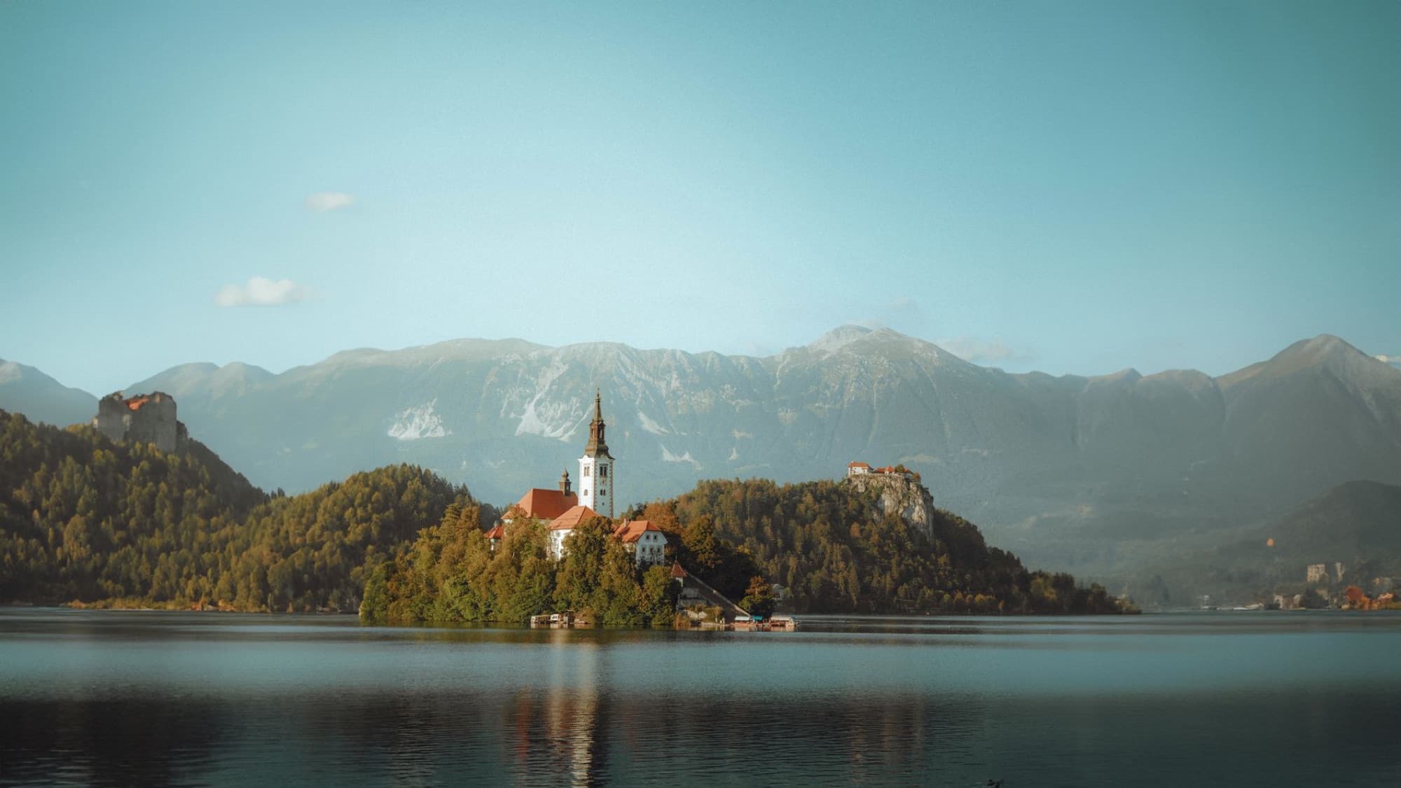 Scenic view of Bled Island with a church in Lake Bled, surrounded by mountains, under a clear sky in Slovenia.