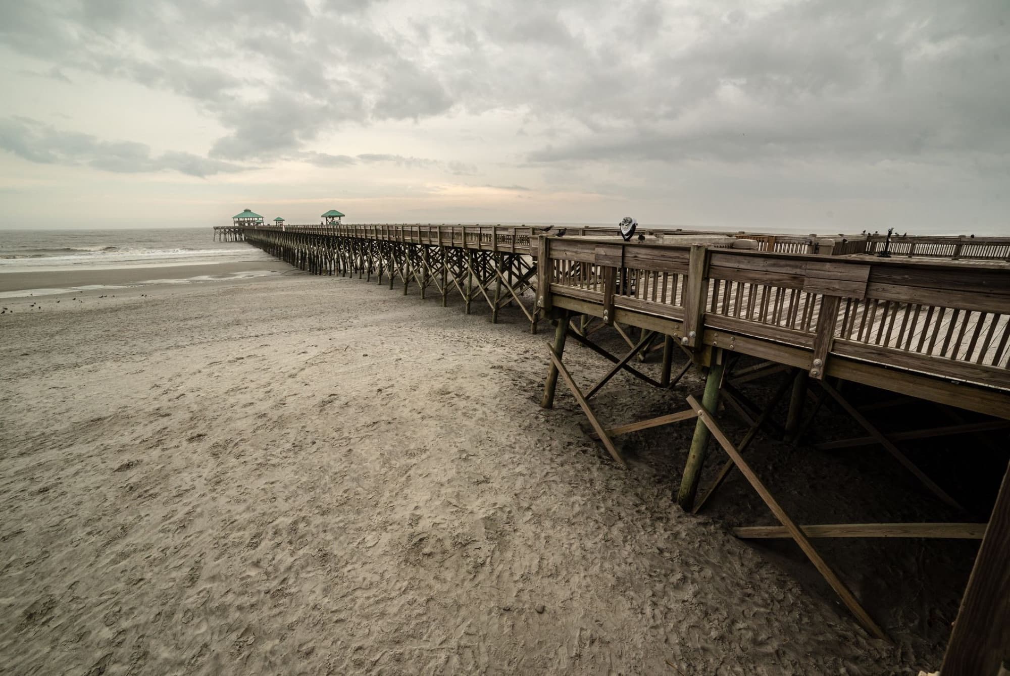 Scenic view of the wooden pier at Folly Beach, South Carolina, under a cloudy sky.