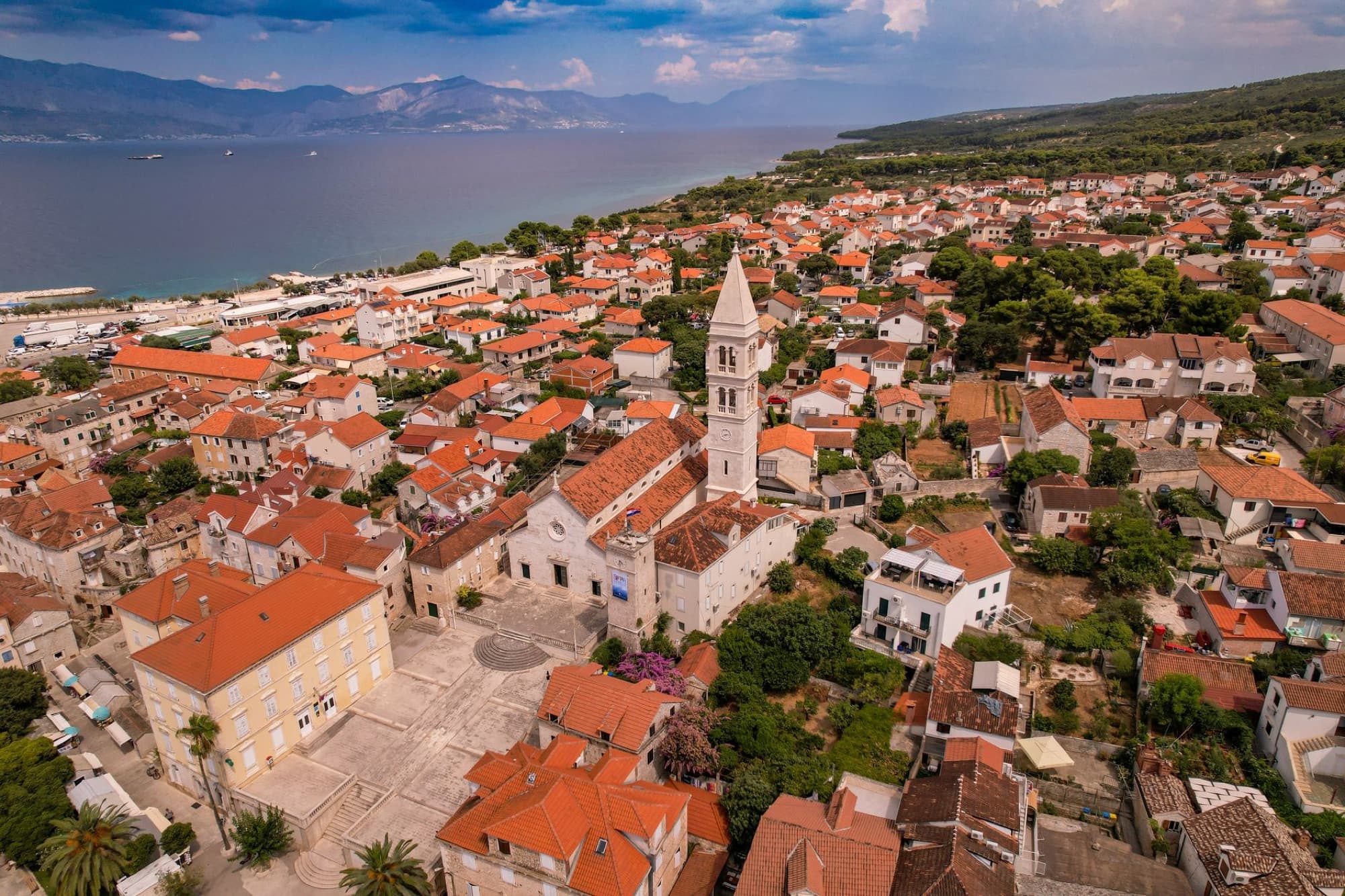 Explore the scenic aerial view of a historic Adriatic coastal town with red rooftops and a prominent church.