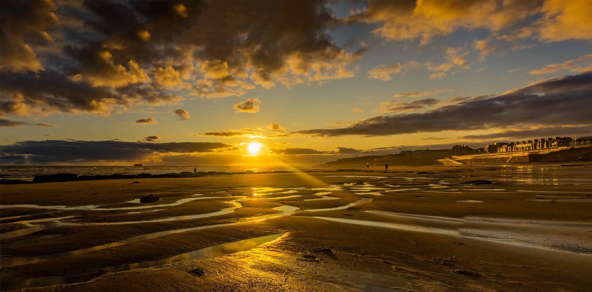 Beautiful sunset over a serene beach with dramatic clouds and golden reflections.