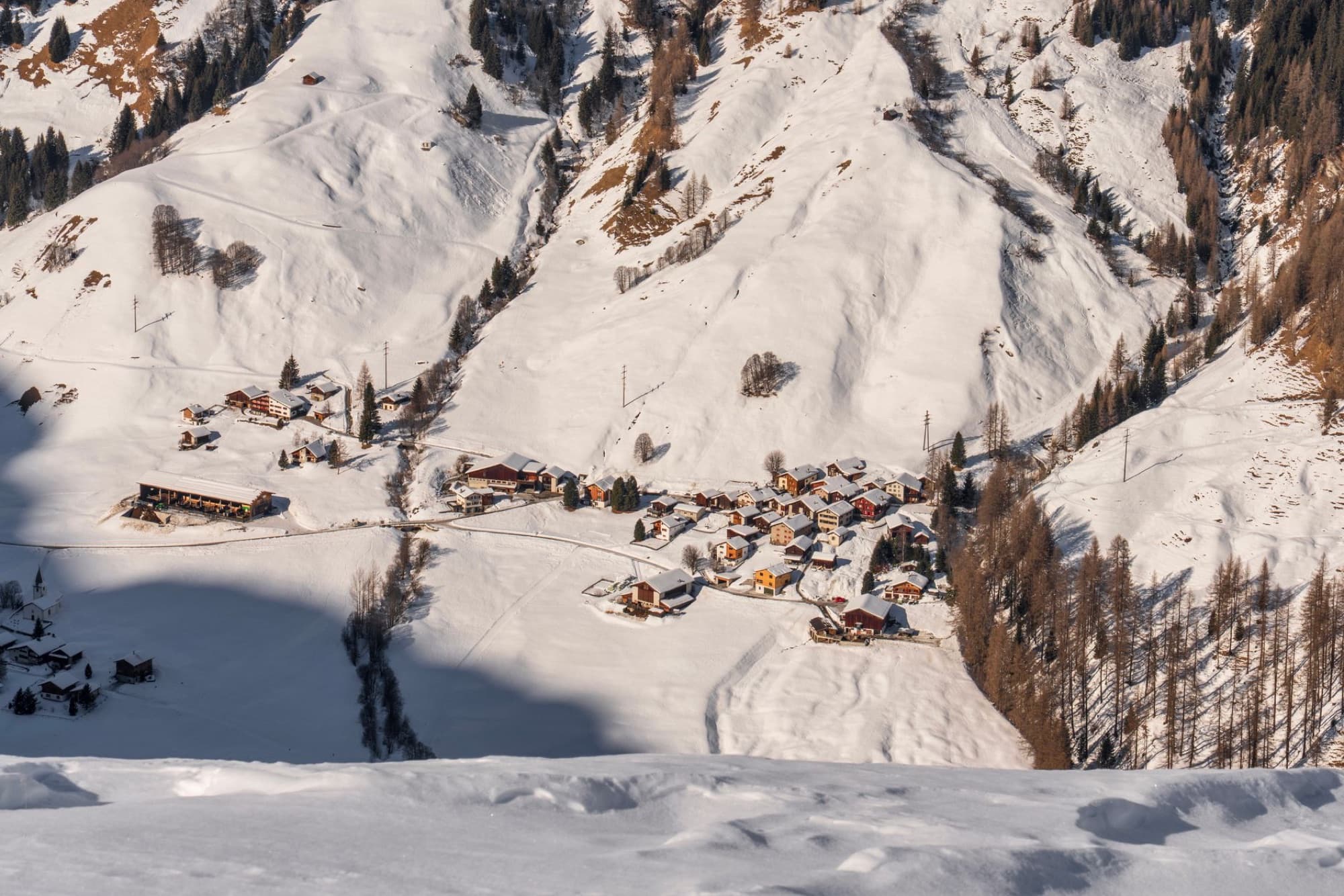 Aerial view of a village nestled in snowy mountains under clear skies.