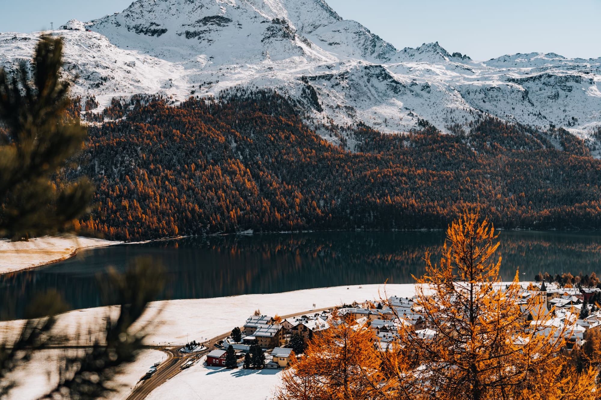 Beautiful autumn landscape with snowy mountains, lake, and village.
