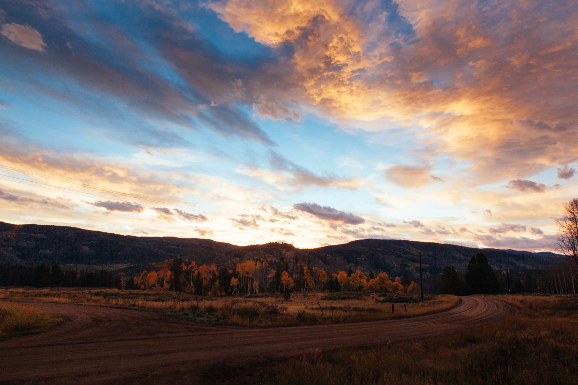 Beautiful sunset over a rural landscape in Steamboat Springs, Colorado with a winding dirt road and autumn foliage.