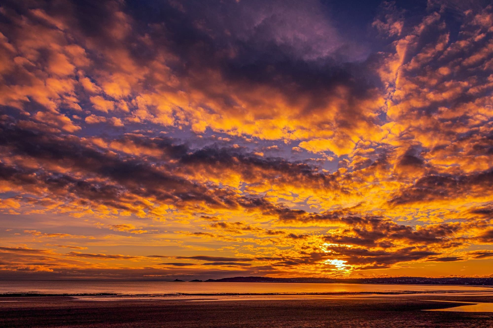 Dramatic sunset with vibrant clouds over Swansea Beach, creating a breathtaking view.