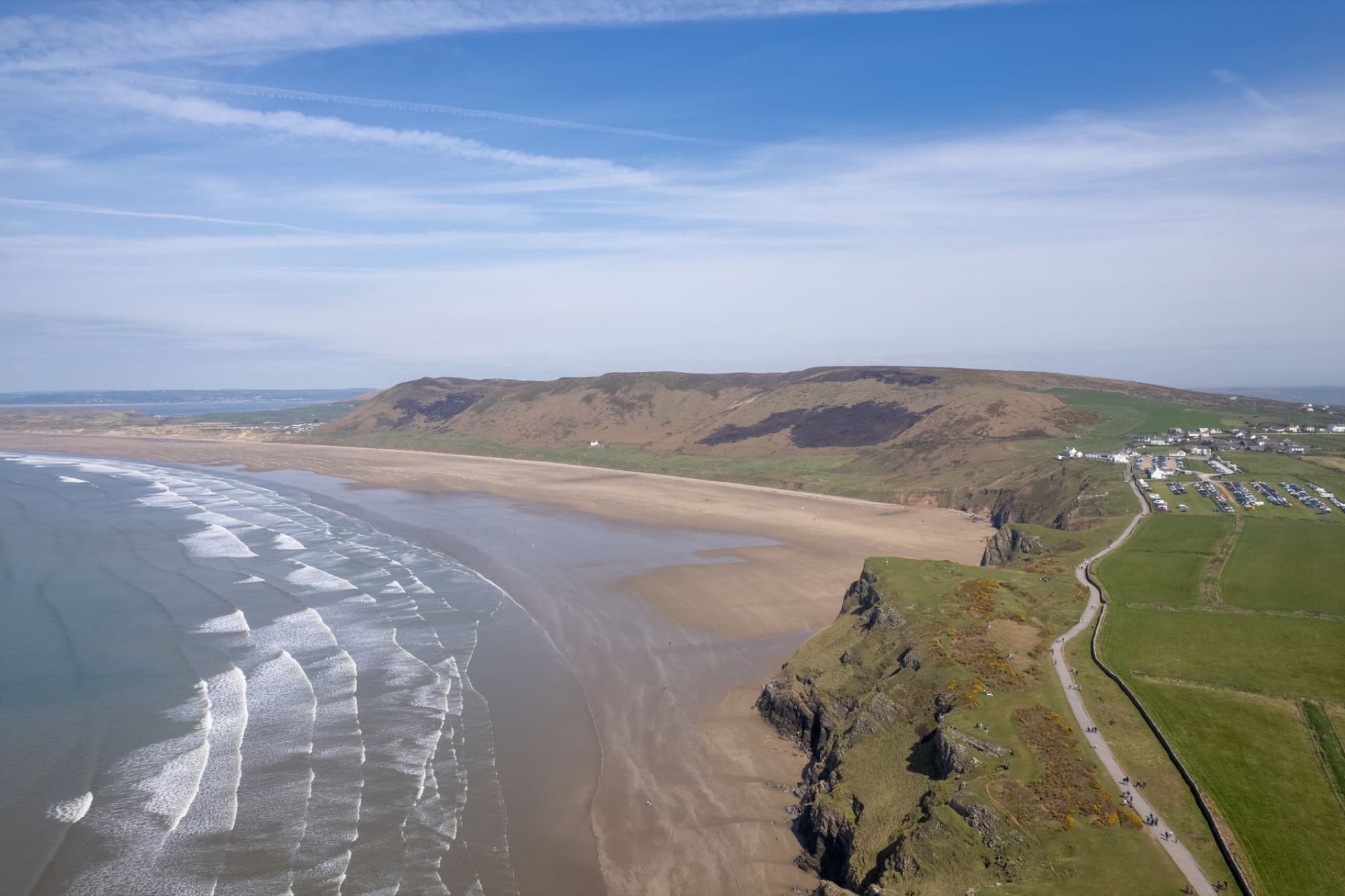 A stunning aerial view of Rhossili Beach, cliffs, and countryside in Wales, showcasing natural beauty and scenic landscapes.