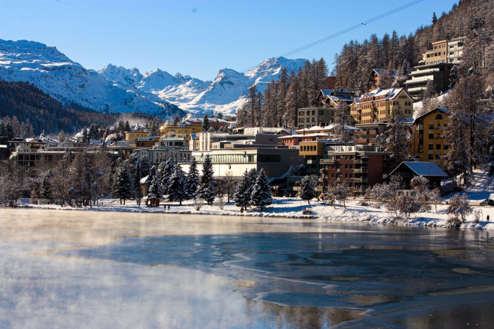 Scenic view of St. Moritz with snowy mountains and frozen lake, in winter.
