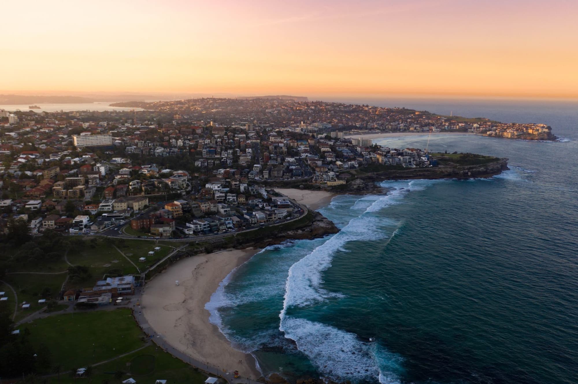 A breathtaking aerial shot of Bronte Beach, NSW, Australia during sunset featuring ocean waves and coastal cityscape.