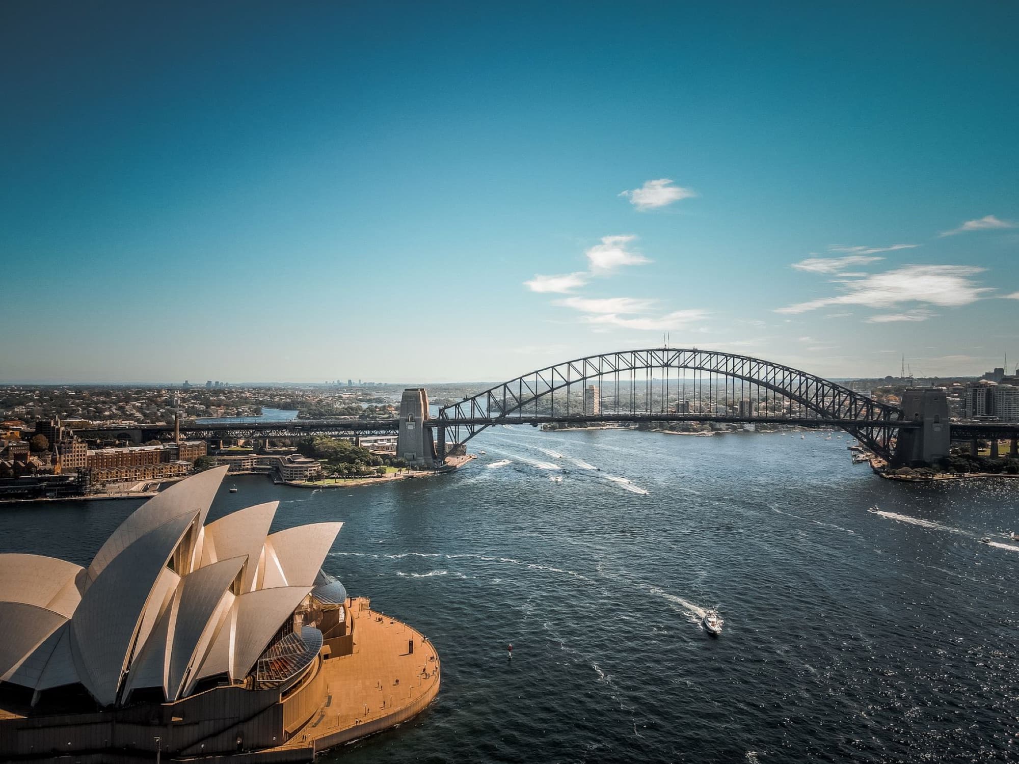 Aerial view of Sydney Harbour featuring the iconic Opera House and Harbour Bridge under a clear blue sky.