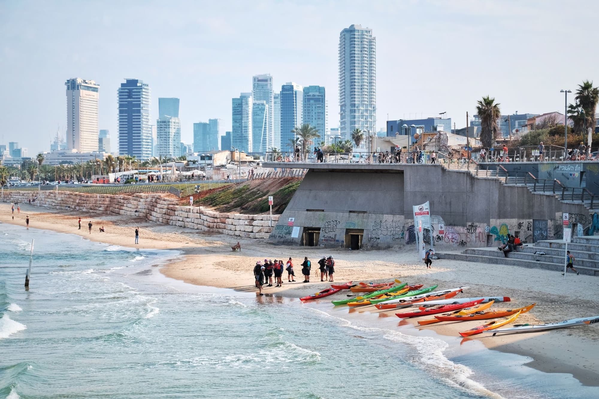 A vibrant beach scene in Tel Aviv featuring kayaks and a modern city skyline.