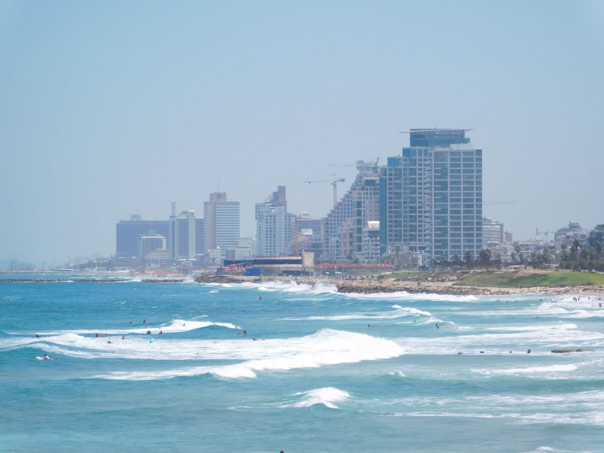Aerial view of Tel Aviv's vibrant beachfront skyline with surfers enjoying the Mediterranean Sea waves.