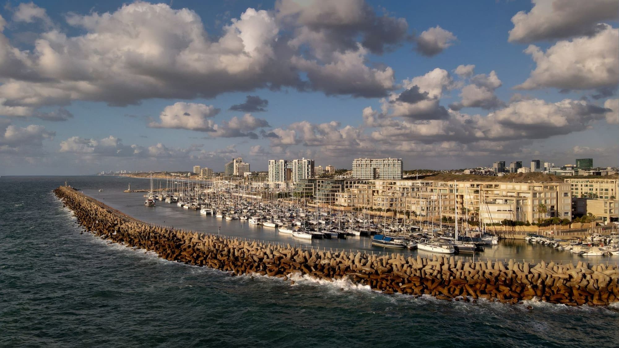 A scenic aerial view of Tel Aviv Marina with yachts docked alongside the breakwater.