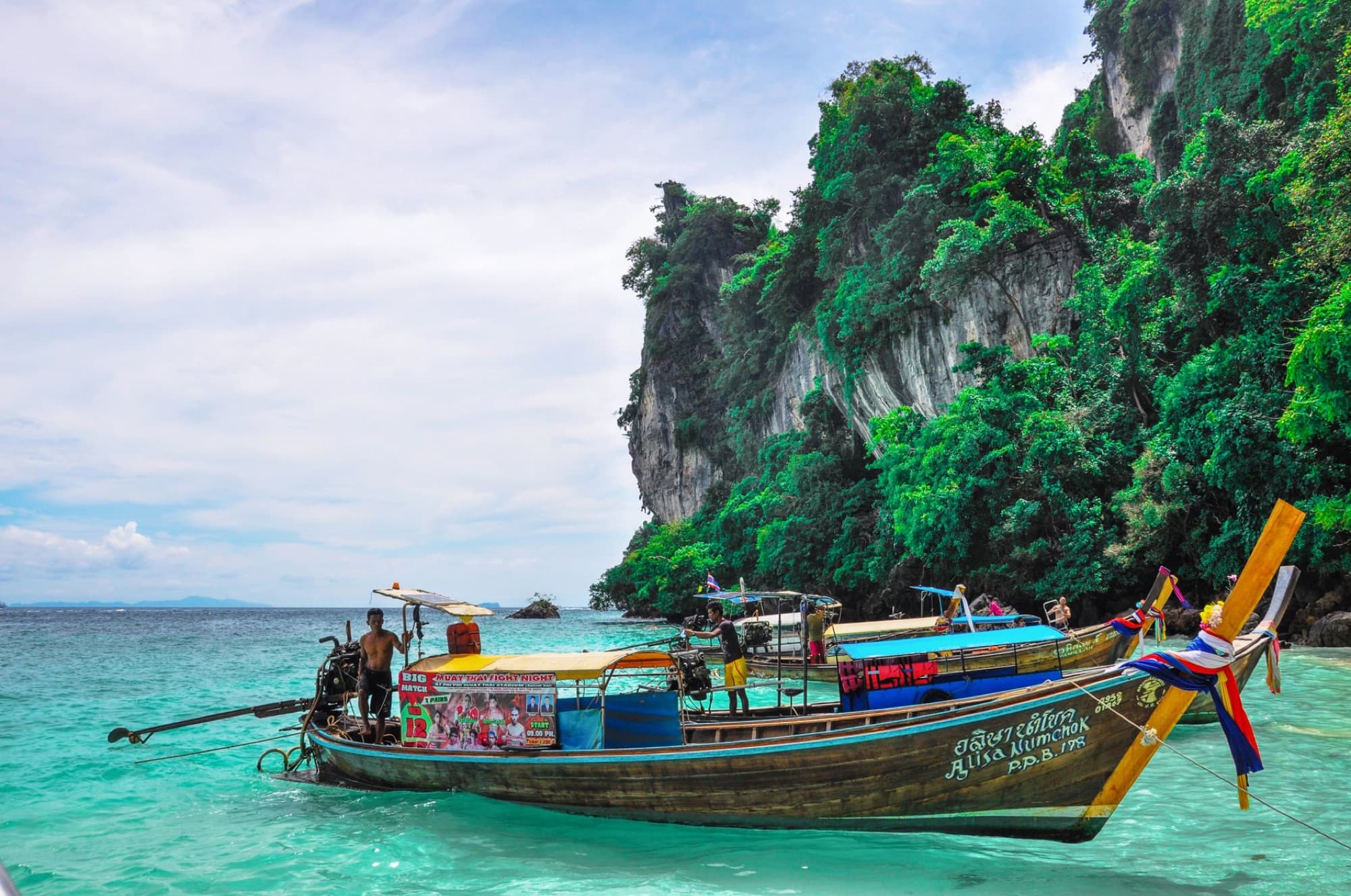 Traditional longtail boat moored in turquoise waters near limestone cliffs in Phang Nga, Thailand.