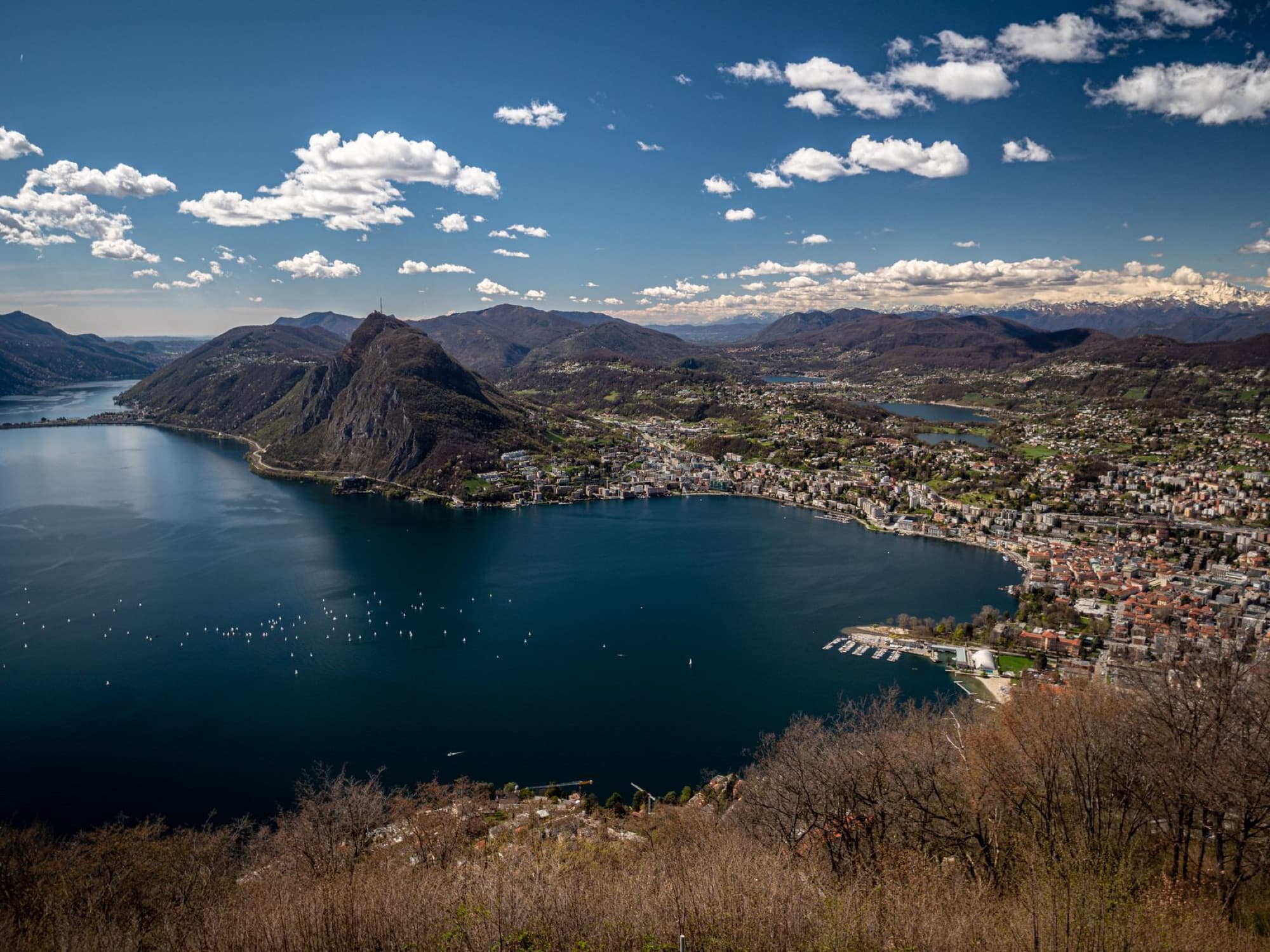 Explore this breathtaking aerial panorama of Lugano city and lake under a clear blue sky.