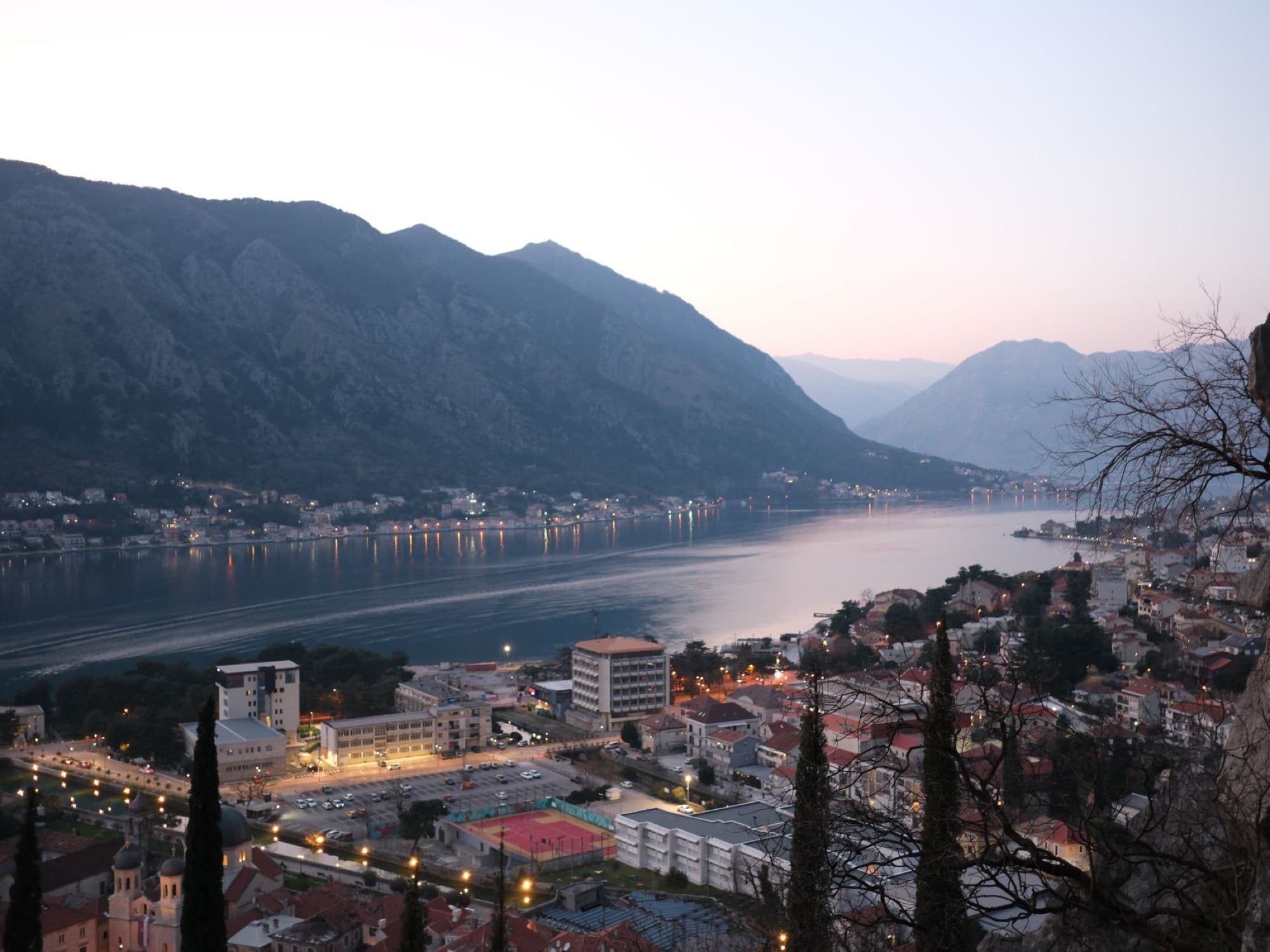 Twilight panorama of Kotor Bay with surrounding mountains and city lights.