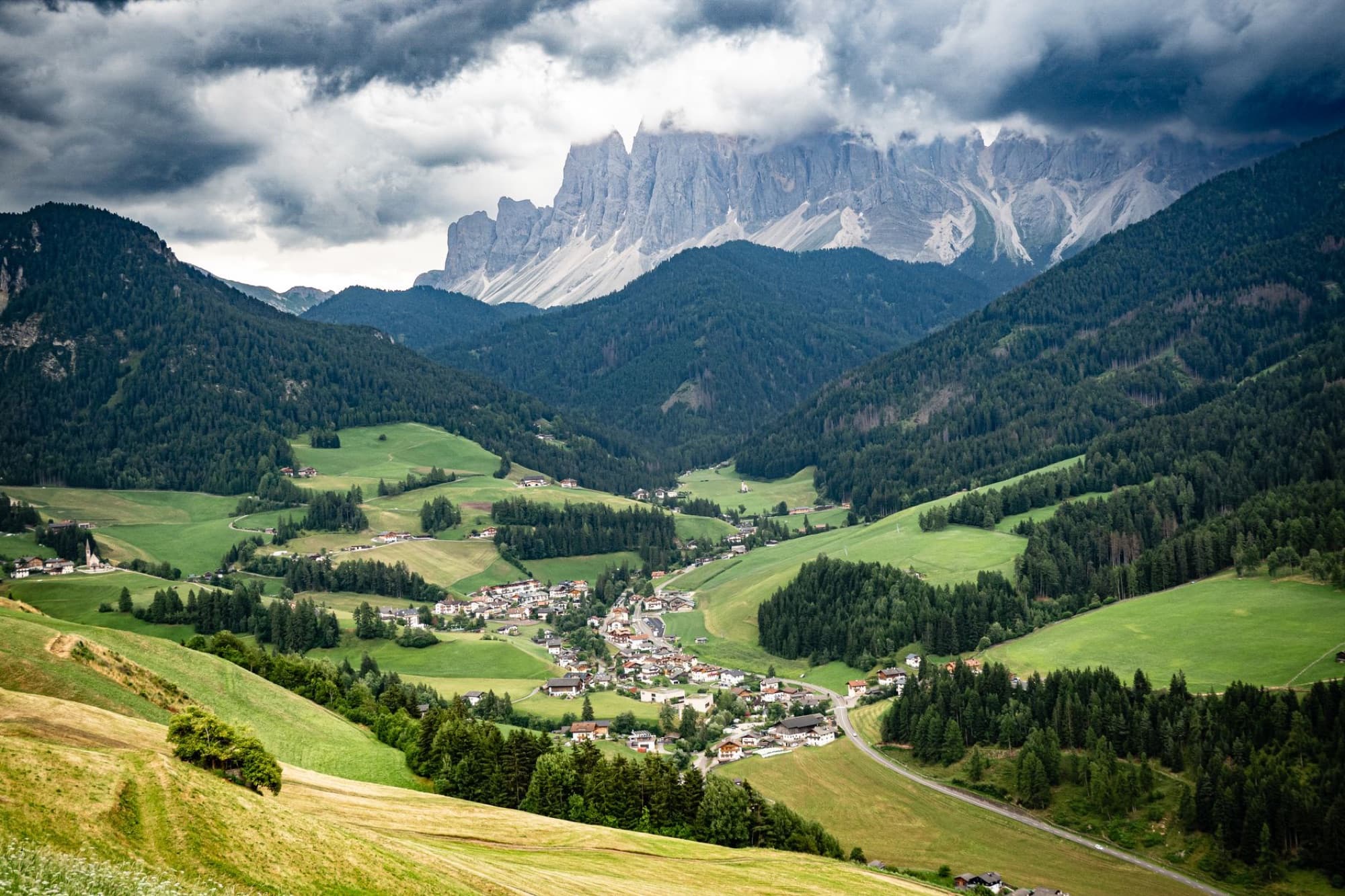 Scenic panorama of a lush green valley with a quaint village nestled amidst towering mountain peaks.