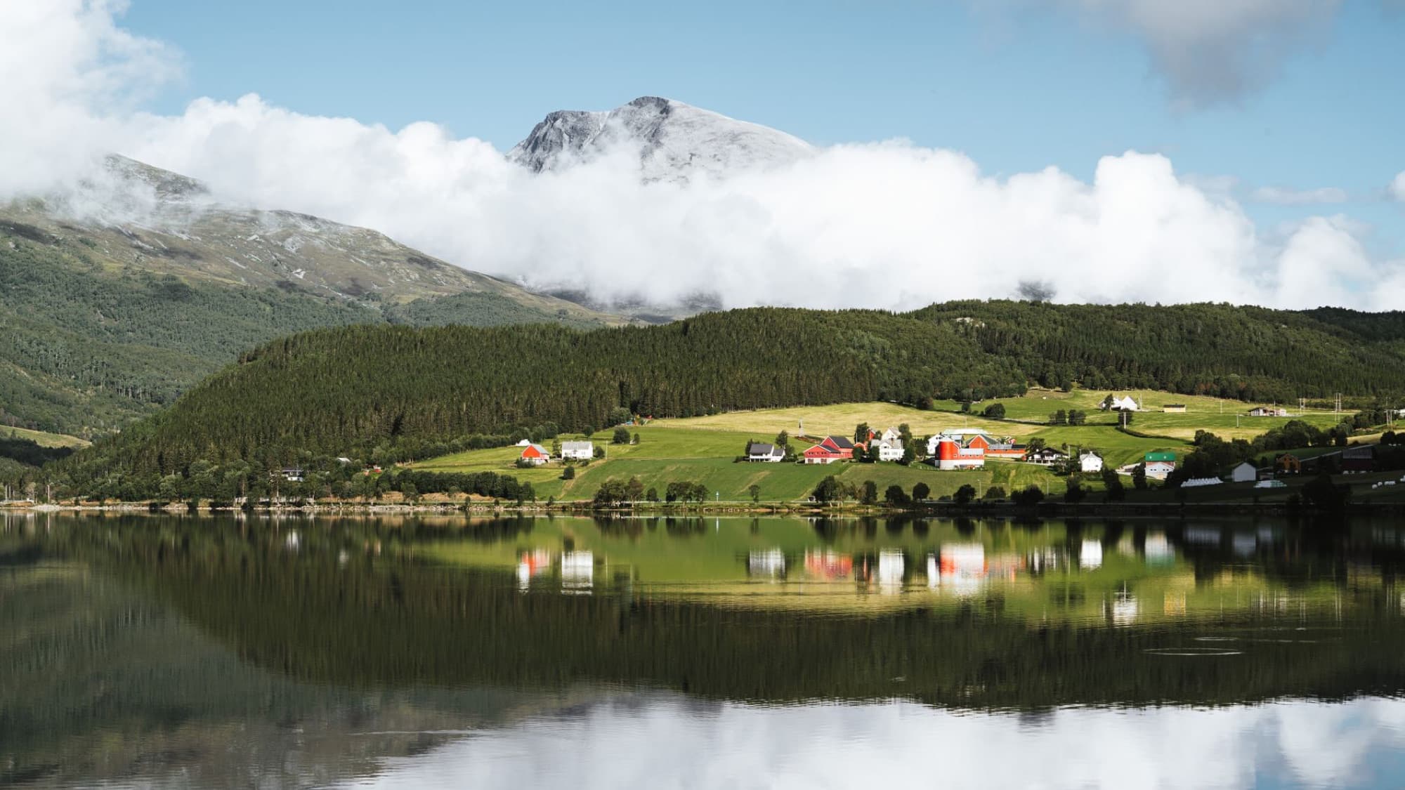 Tranquil Norwegian landscape featuring hills, a mountain, and reflective lake.