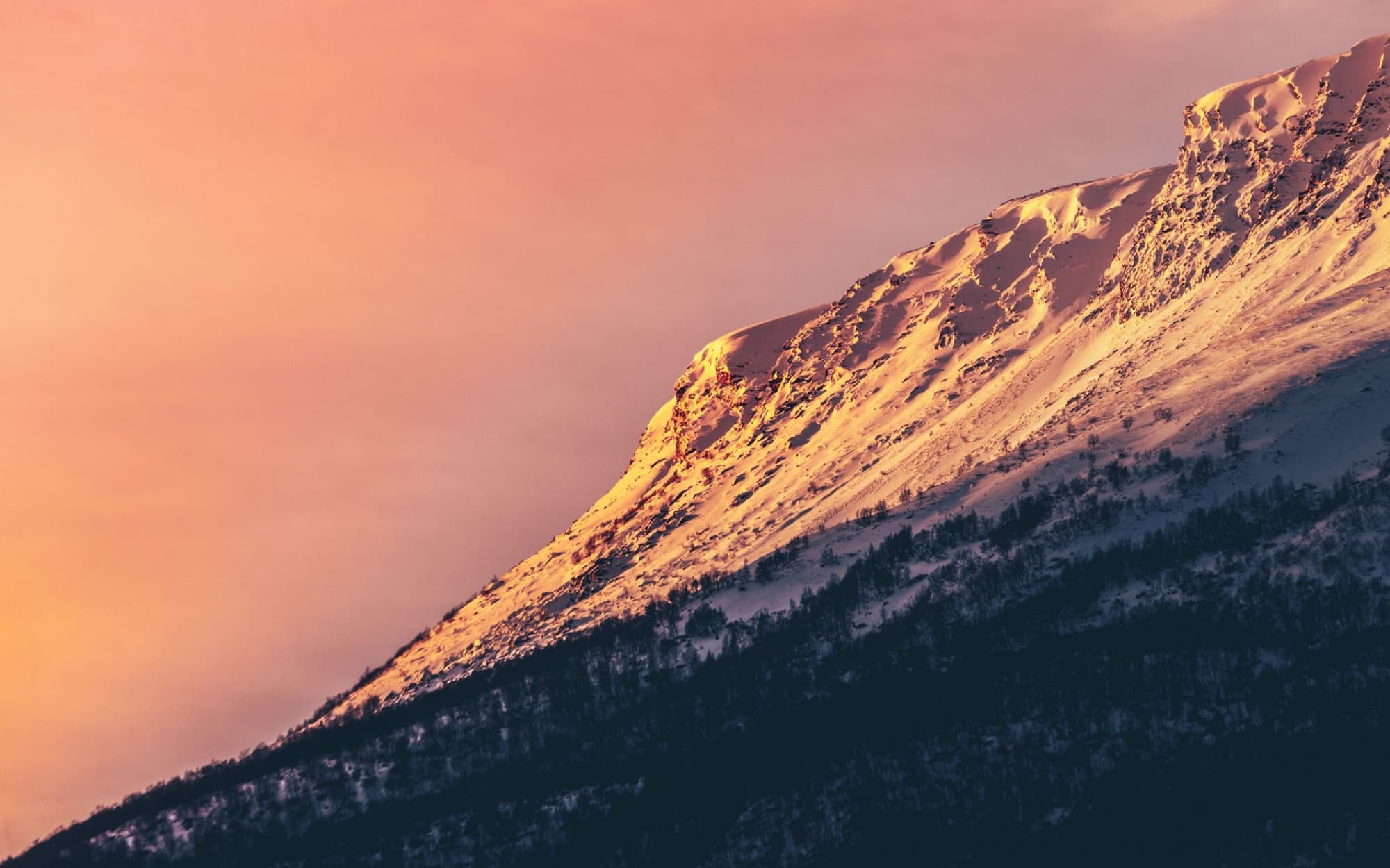 Captivating view of a snow-covered mountain peak at sunset in Norway with a warm, dramatic sky.