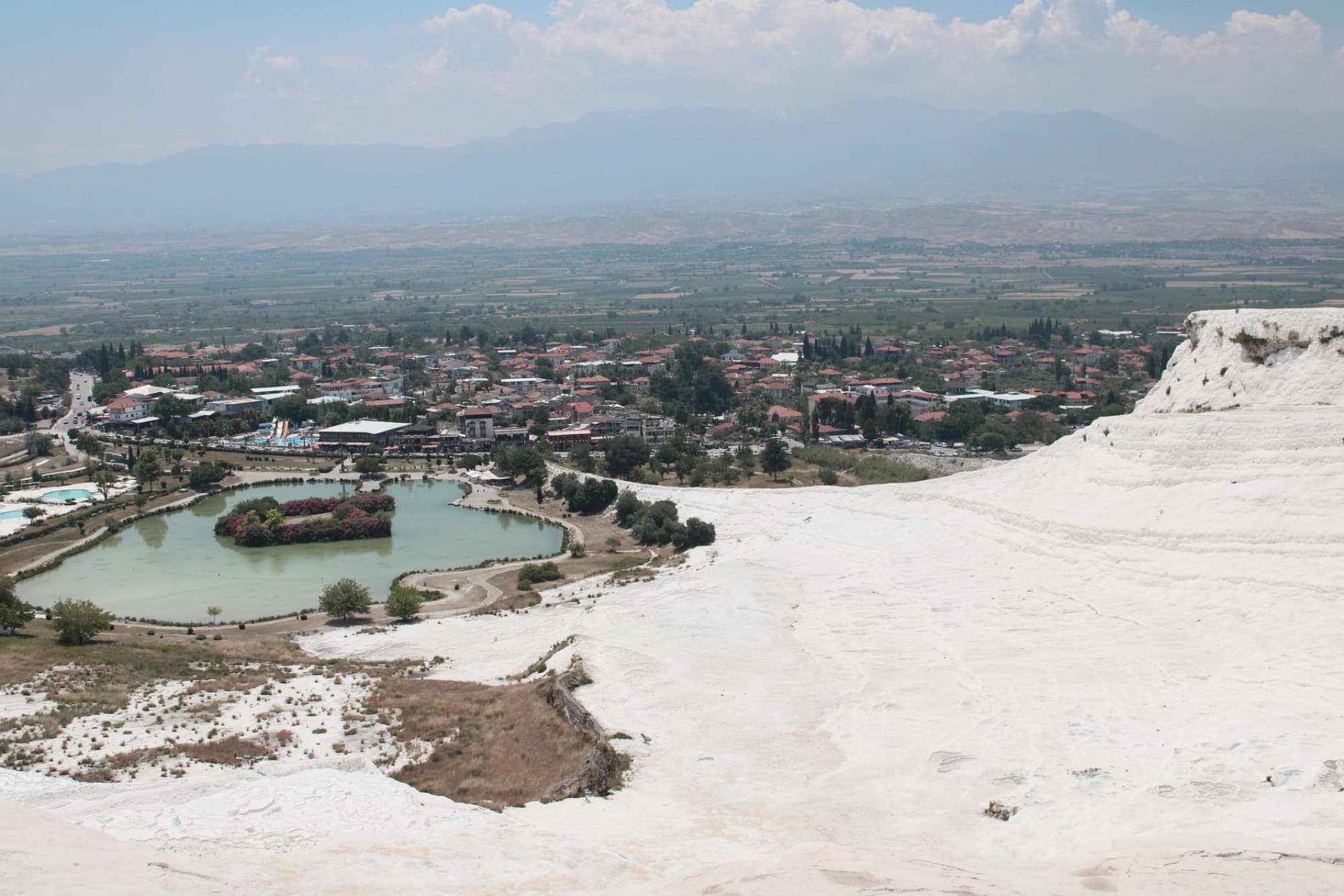 Aerial shot of Pamukkale's white travertines and lush landscape under a clear sky.