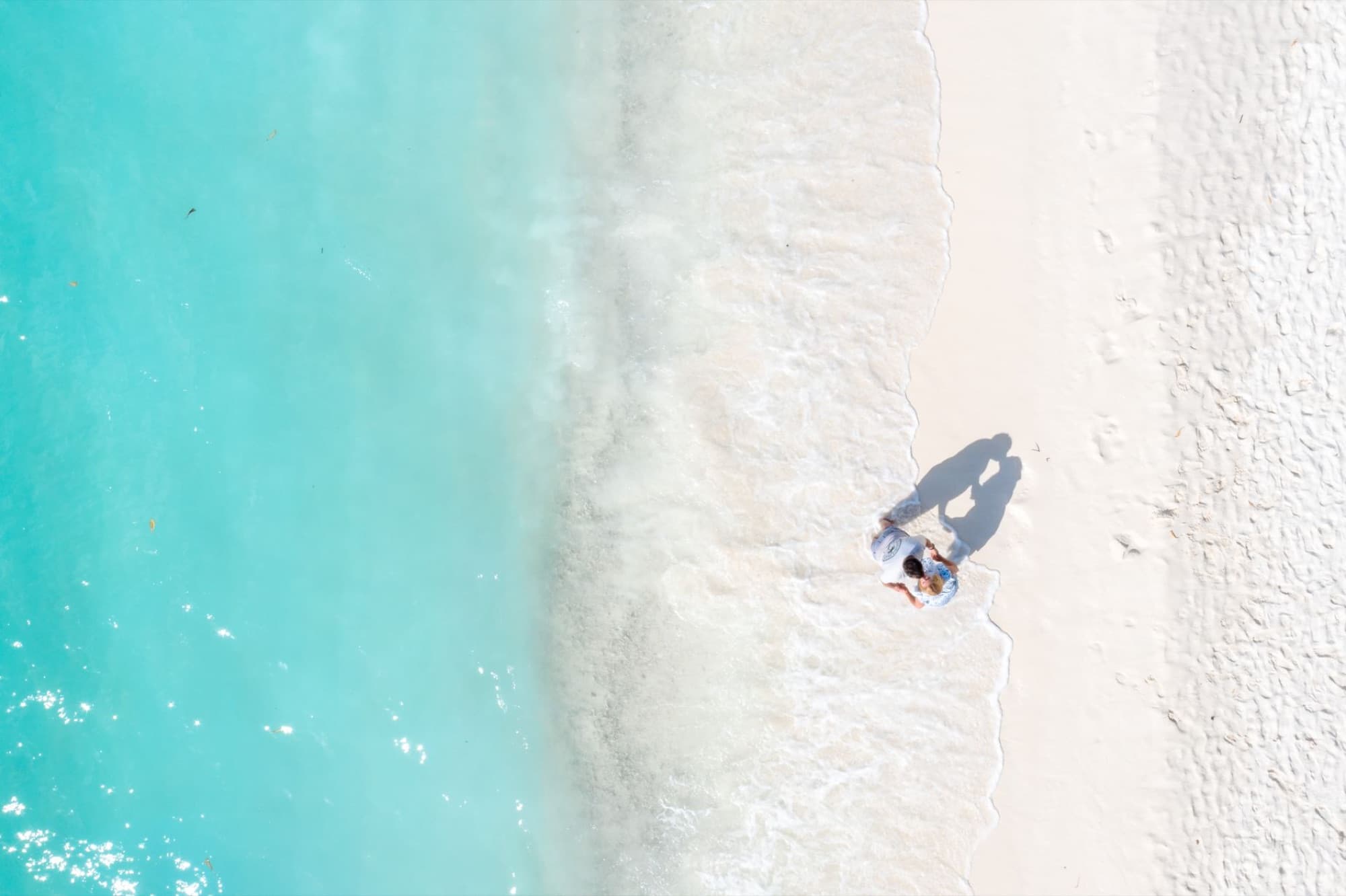 Aerial view of a couple embracing on a beautiful beach in the Maldives, with turquoise water and soft sand.