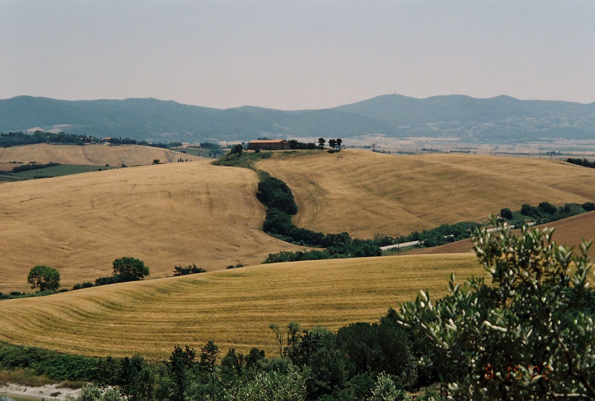 A picturesque landscape of the rolling hills in Tuscany, showcasing golden fields and distant mountains.