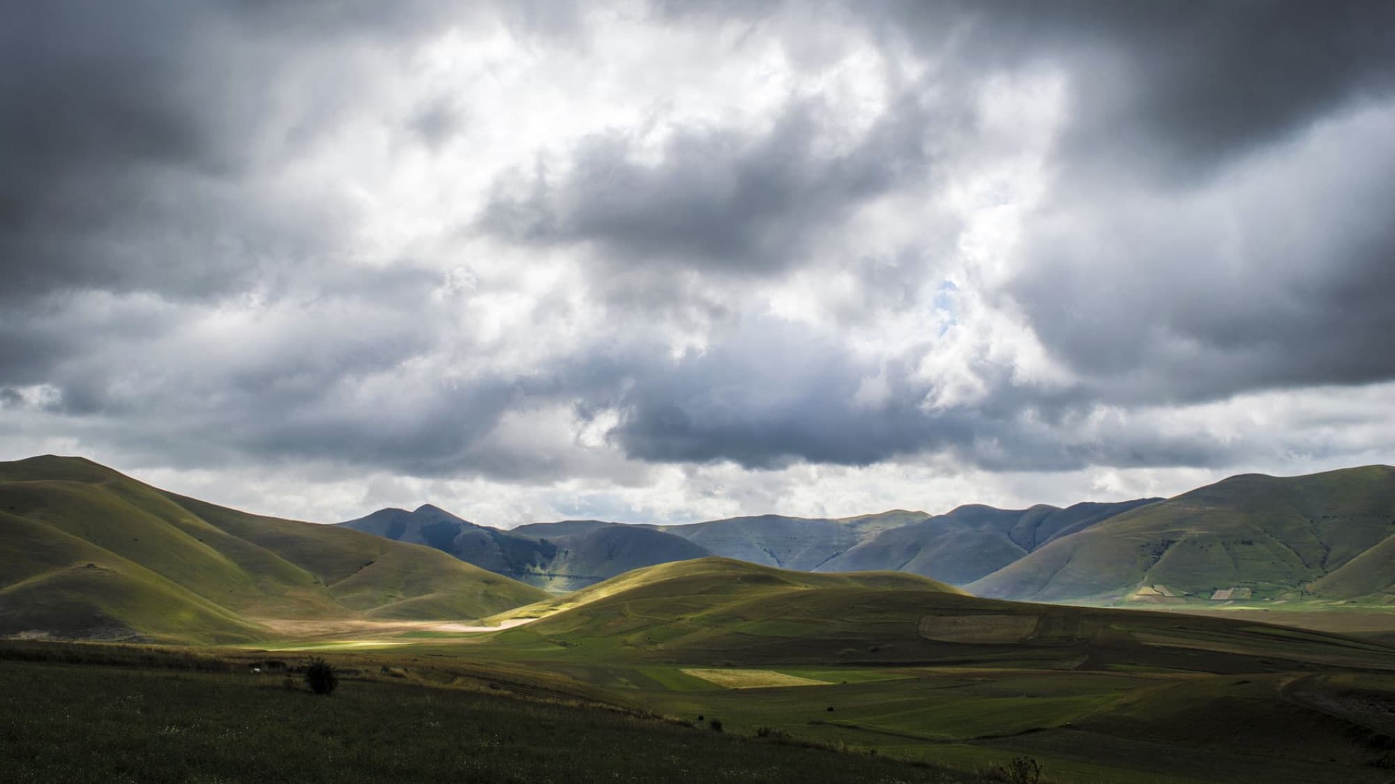 Scenic landscape of Castelluccio hills under dramatic clouds in Umbria, Italy.
