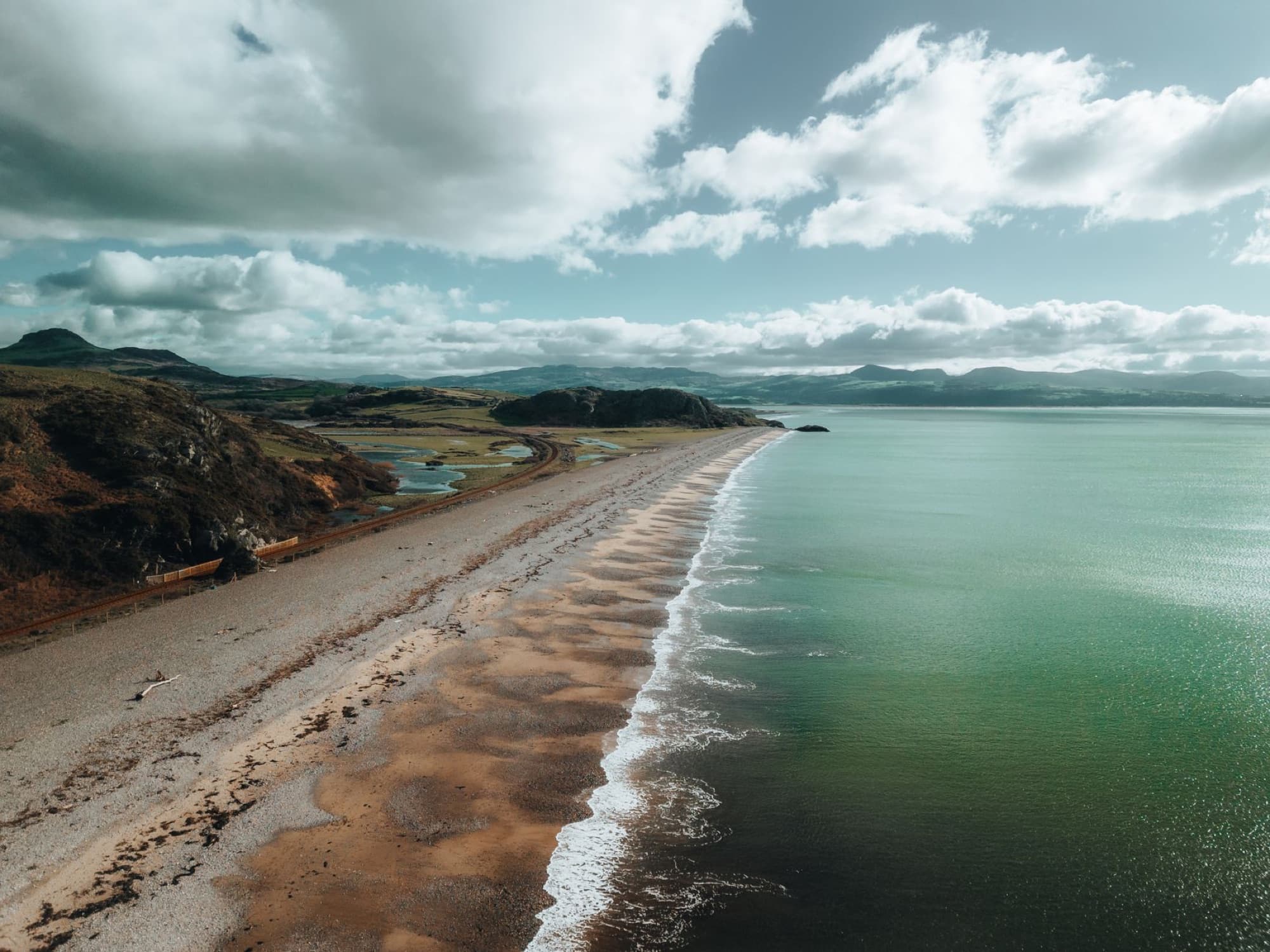 Breathtaking aerial view of the scenic beach and coastline in Gwynedd, Wales, under a cloudy sky.