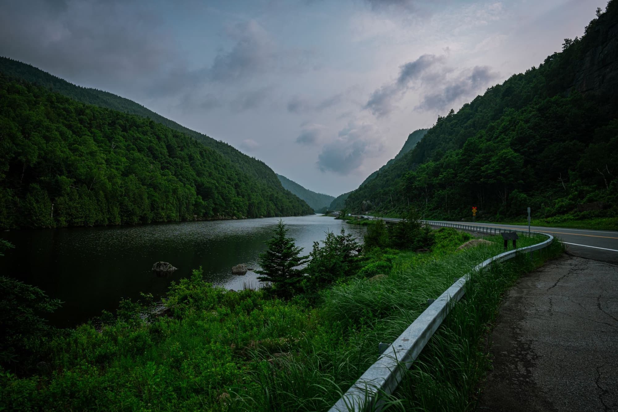 Lush green valley with river, mountains, and a scenic road curve.