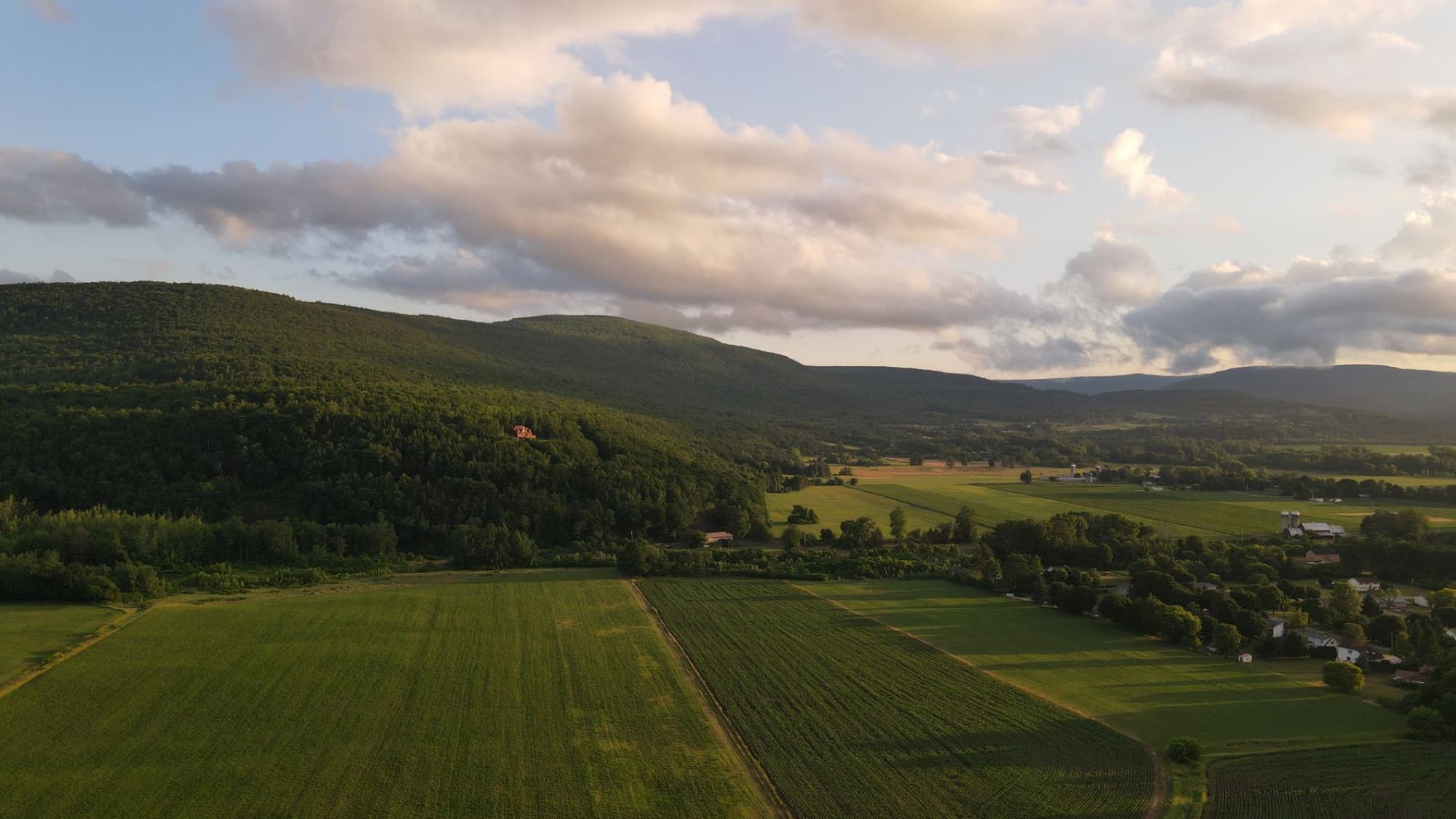 Scenic aerial view over lush fields and rolling hills in Middleburgh, NY, at sunset.