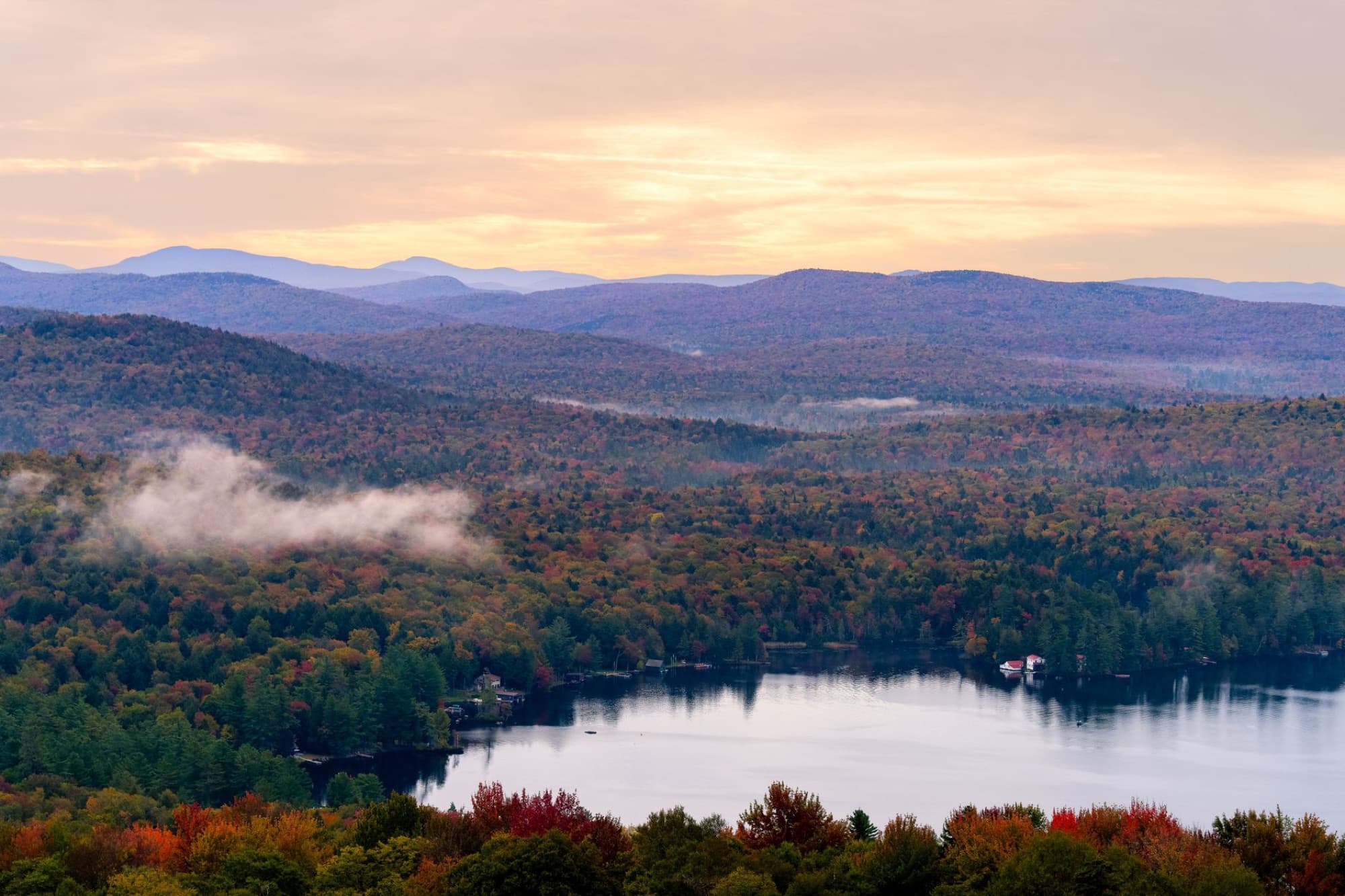 Breathtaking view of Adirondack Mountains with vibrant autumn colors at sunrise over a serene lake.