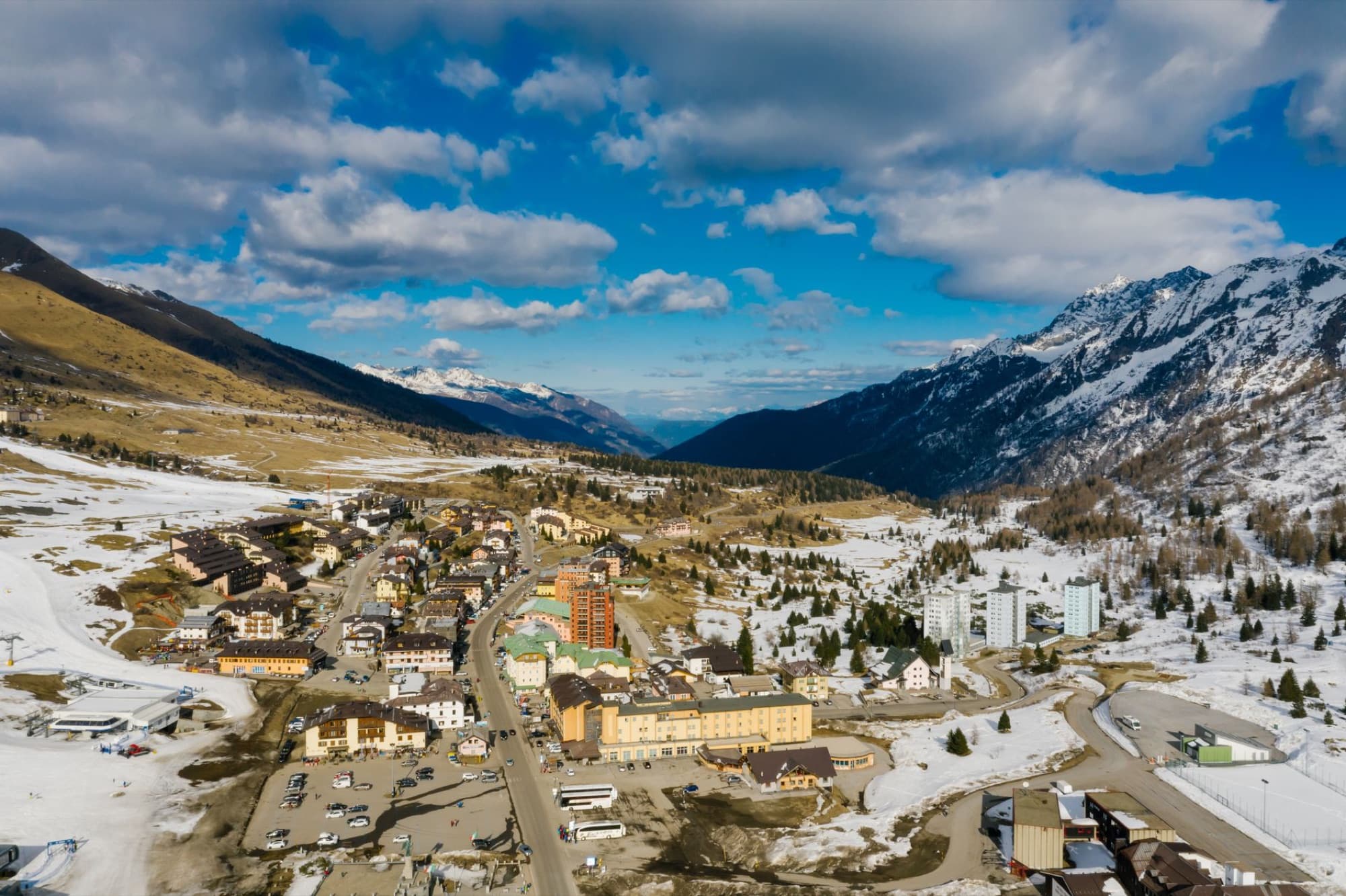 Aerial view of a quaint mountain town surrounded by snow-capped peaks under a blue sky.
