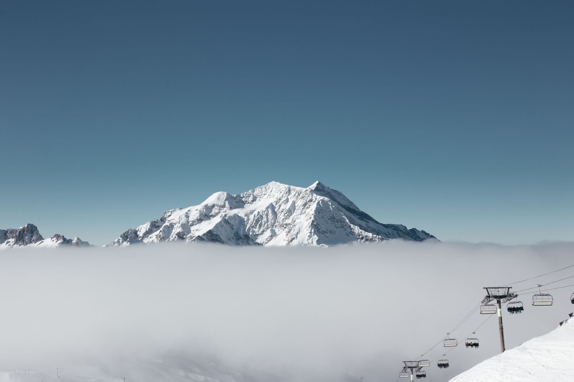 Snowy Mont Blanc above fog with ski lifts in Val-d'Isère, France.