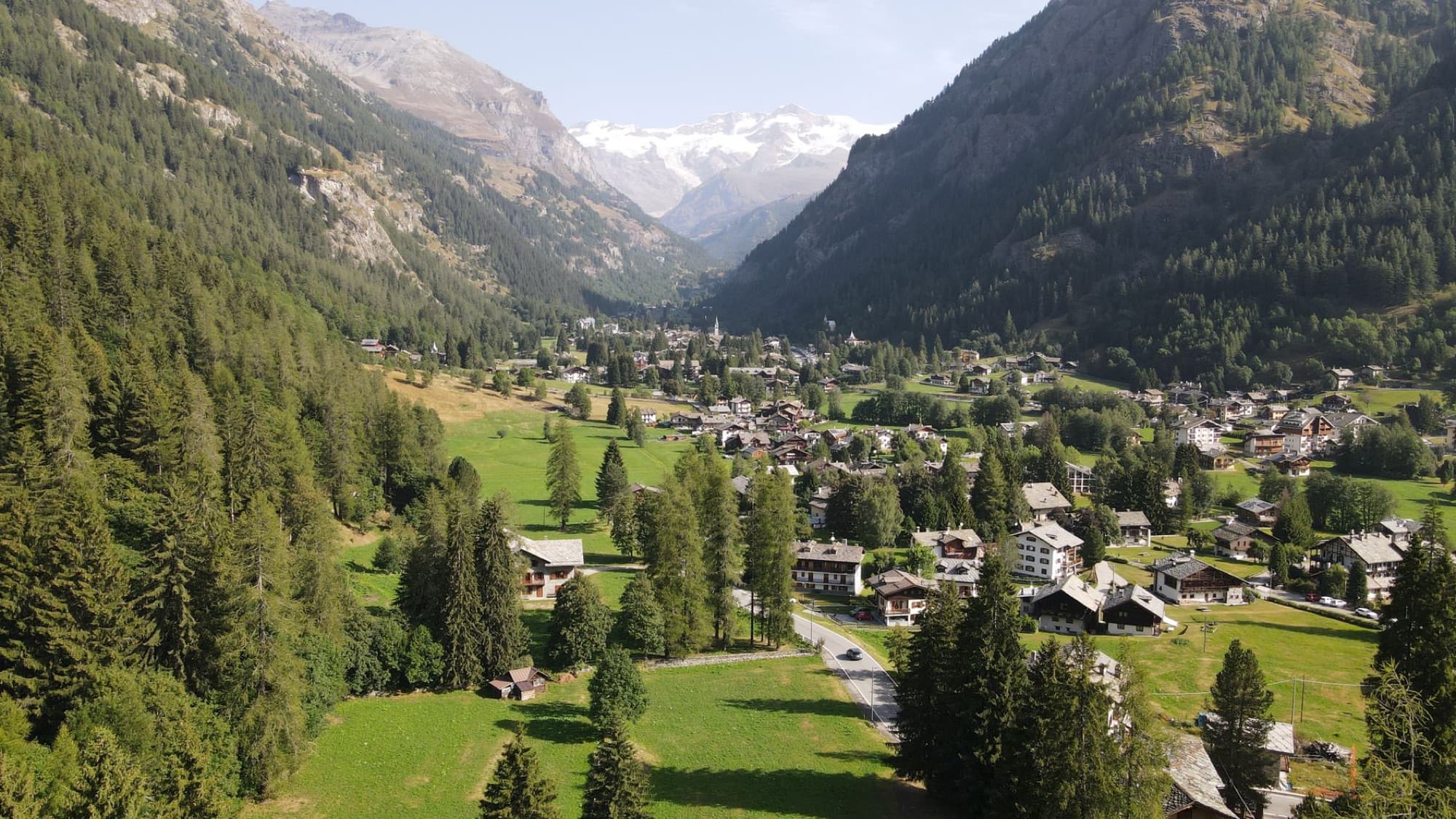 Aerial view of a picturesque alpine valley with a charming village nestled among lush greenery and towering mountains.
