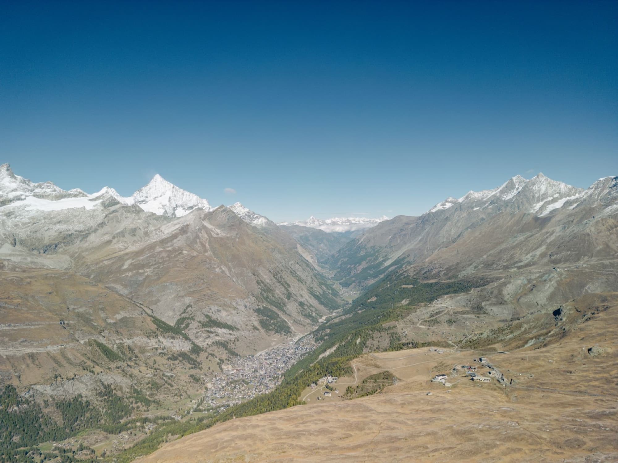 Idyllic aerial view over the Swiss Alps and Zermatt valley with snow-capped peaks under a clear blue sky.
