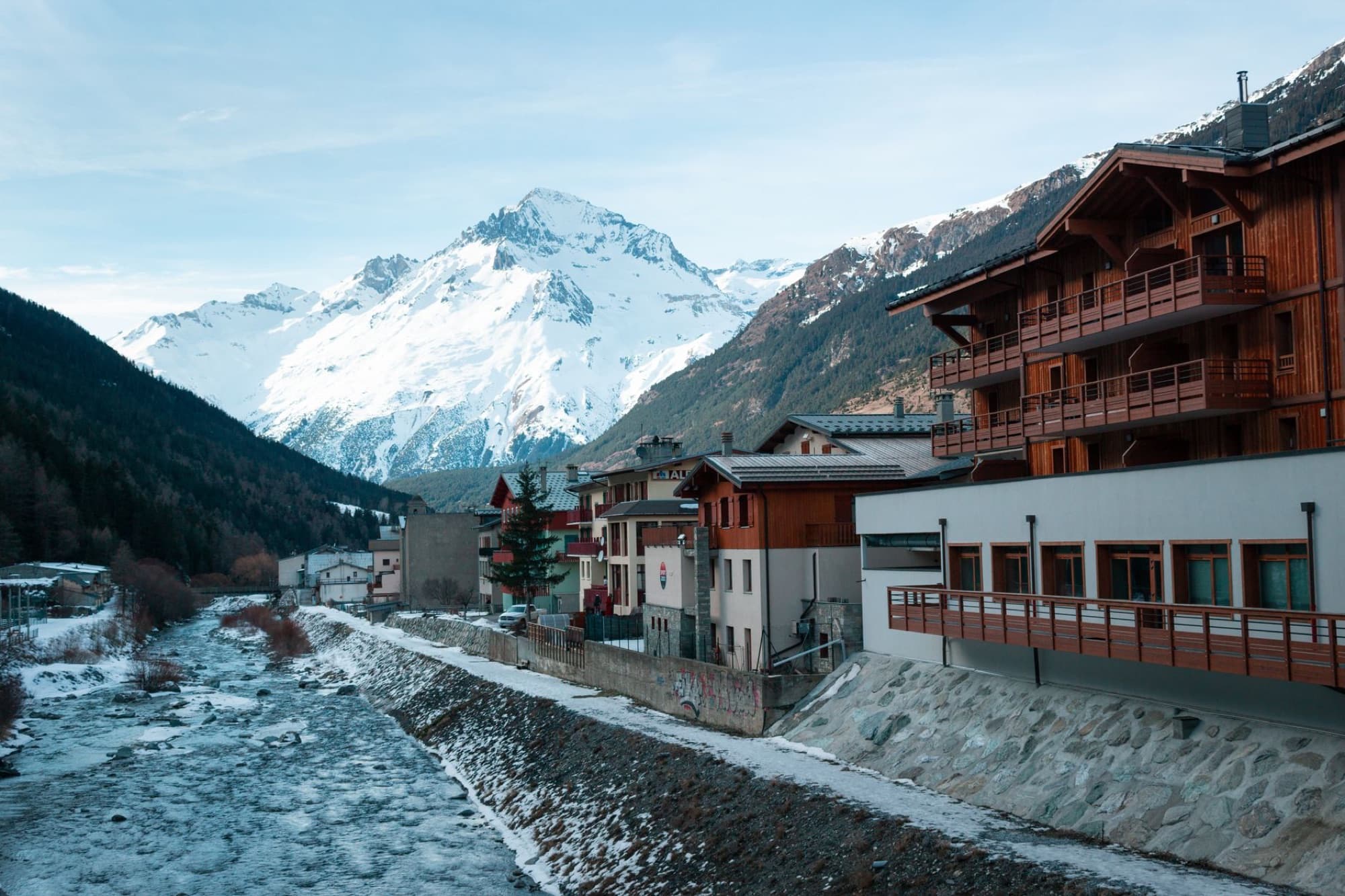 A serene alpine village with snow-capped mountains and charming wooden chalets along a flowing river.
