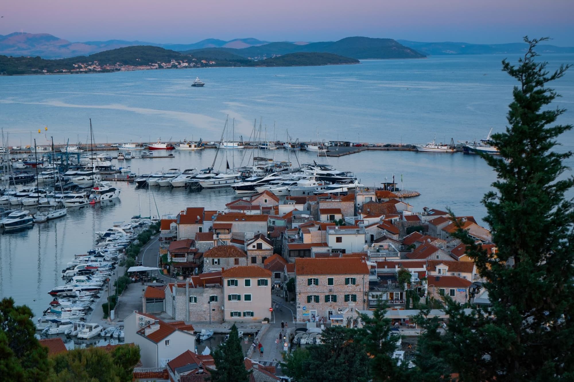 Scenic view of a marina and coastal town at twilight with boats docked and calm waters.