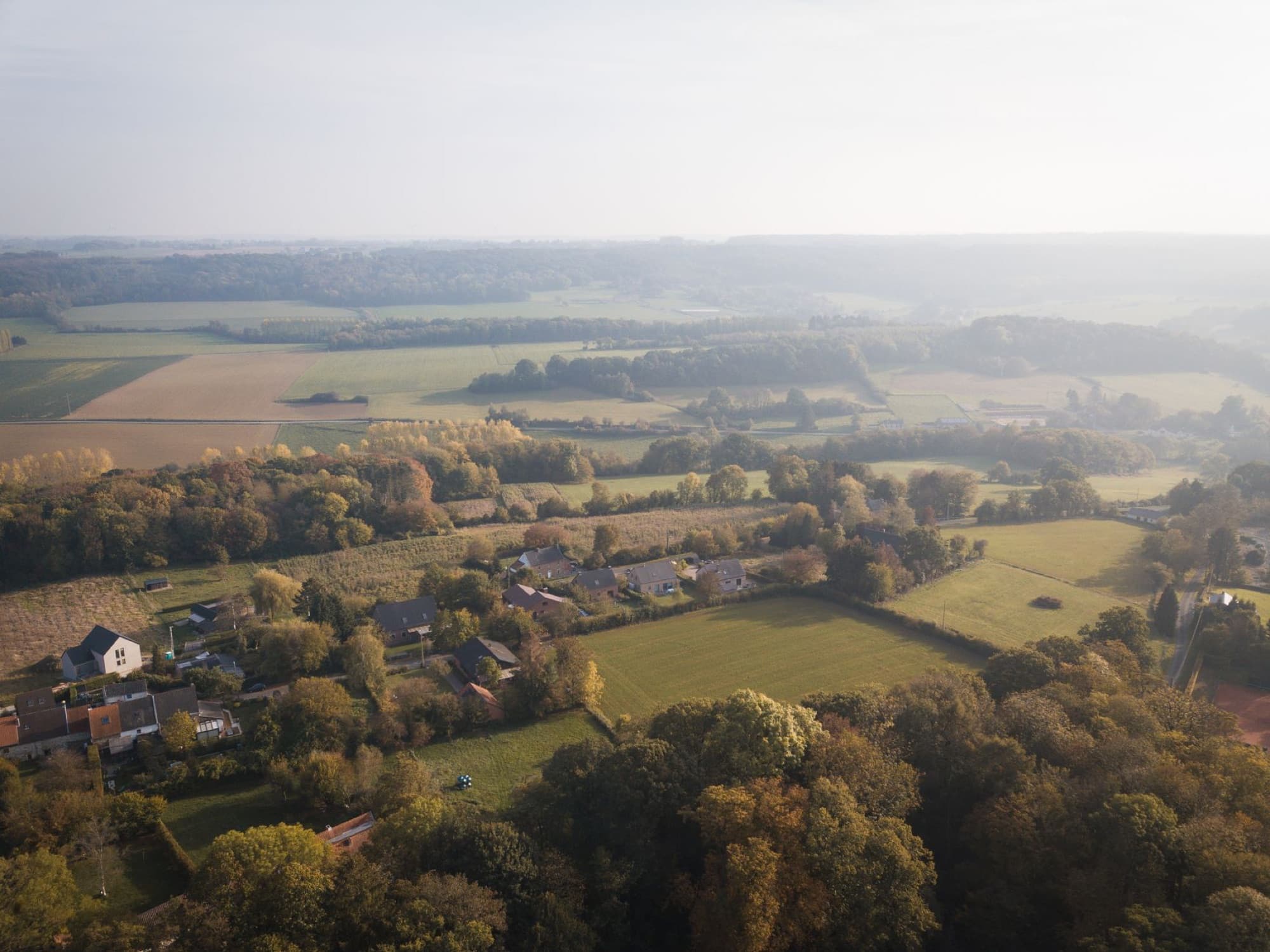 Scenic aerial drone view of a serene countryside landscape featuring fields, forests, and houses during daylight.