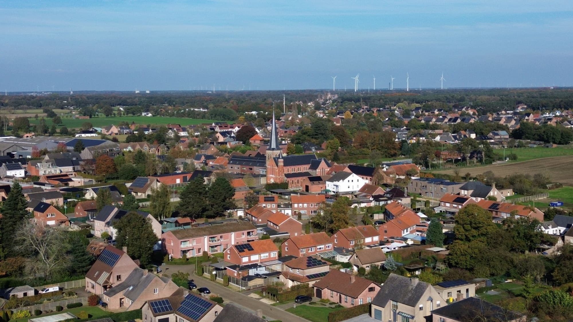 A picturesque aerial view of a quaint Flemish village in Belgium during autumn with wind turbines on the horizon.
