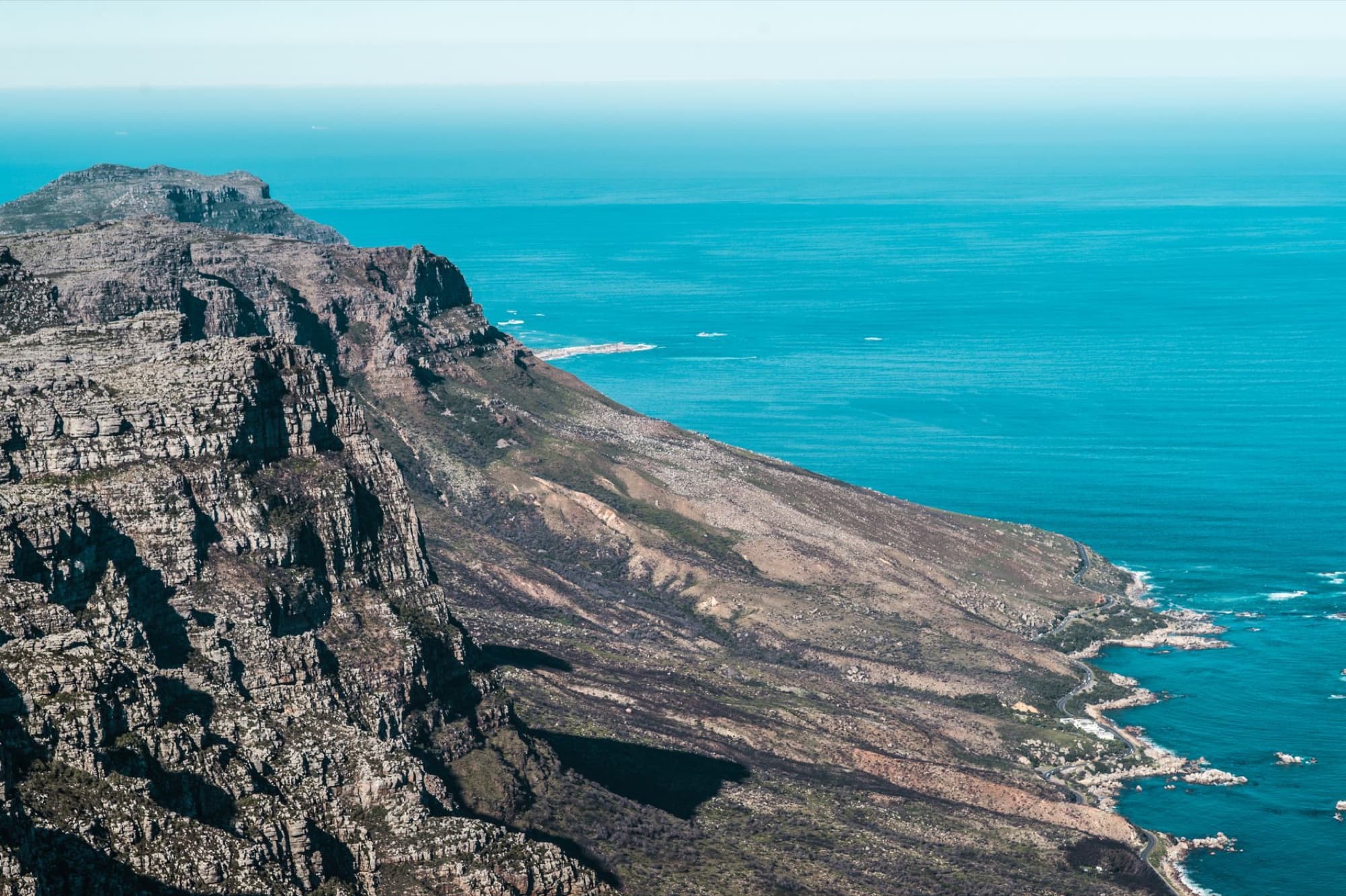 Stunning aerial view of Table Mountain's rocky cliffs meeting the ocean in Cape Town, South Africa.