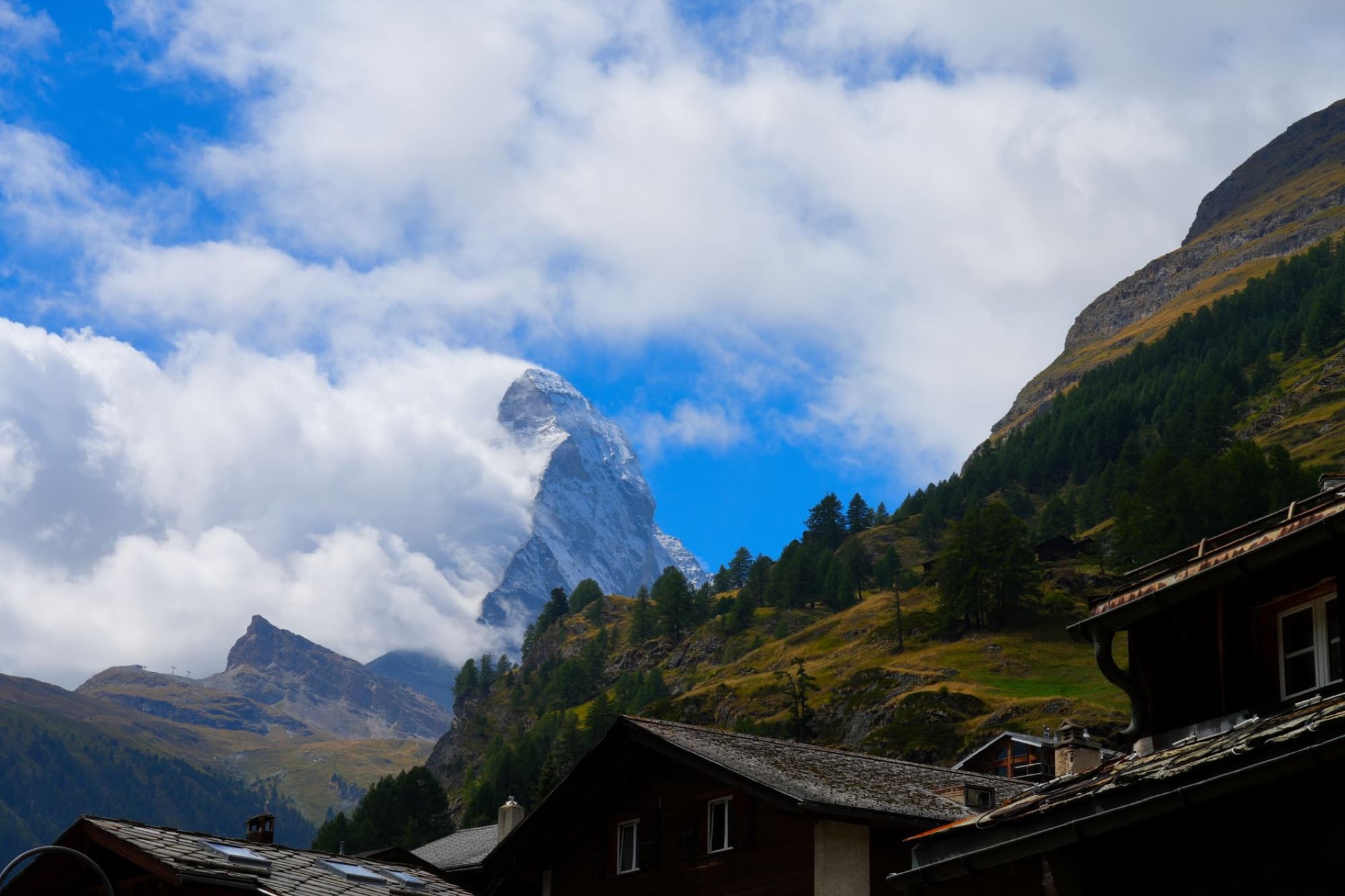 Breathtaking scene of the Matterhorn peak surrounded by clouds, viewed from a village in Zermatt.