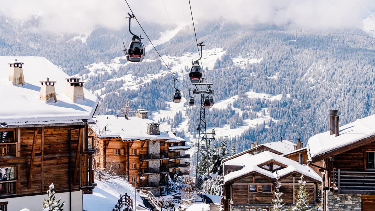 Gondolas rising over snow-covered chalet rooftops in the Alps